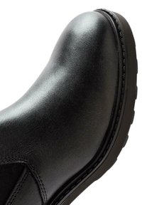 Black leather boot with a rounded toe, elastic side panels, and a textured surface. Features a thick rubber sole with a tread pattern.