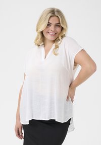 Haut blanc léger avec un décolleté en V et des manches courtes, présentant une texture légèrement transparente et un ourlet asymétrique.