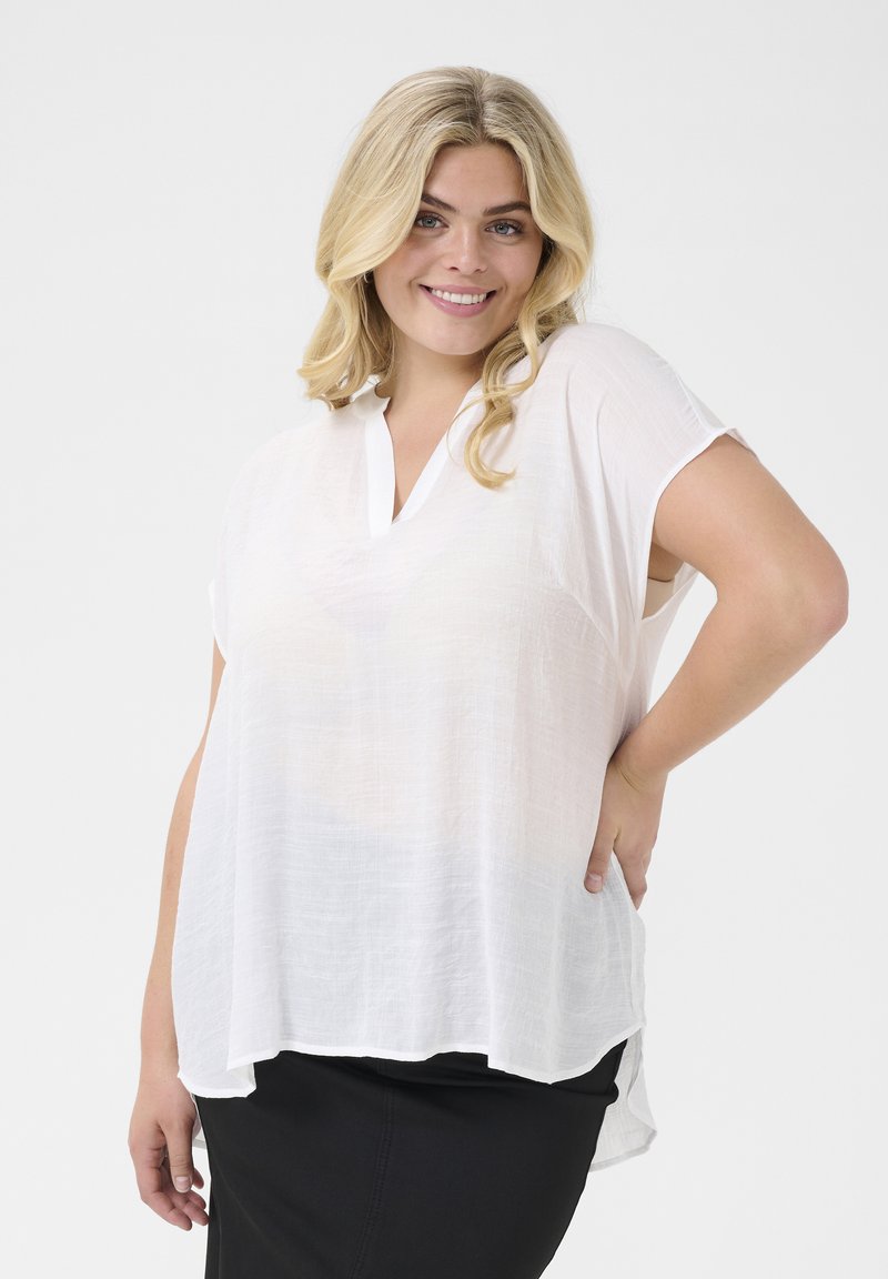 Haut blanc léger avec un décolleté en V et des manches courtes, présentant une texture légèrement transparente et un ourlet asymétrique.