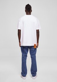 Baltas kokvilnas T-krekls ar brīvu piegriezumu un īsām piedurknēm, saskaņots ar ziliem džinsu biksēm. Ievērības cienīga oranža birka sānu šuvē.