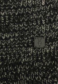 Un tejido de punto en negro y gris presenta un patrón texturizado con un parche de logo tejido que muestra un cráneo de cabra en la esquina inferior.