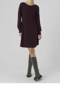 Stickad klänning i djup burgundy med en avslappnad passform, långa ärmar och rundad hals. Bärs med höga, mörkgrå stövlar. Subtil textur synlig.