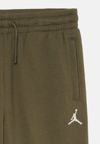 Olive zelené teplákové nohavice vyrobené z mäkkej tkaniny, s elastickým pásom, šnúrkou, bočnými vreckami a bielym logom Jumpman ako akcentom.
