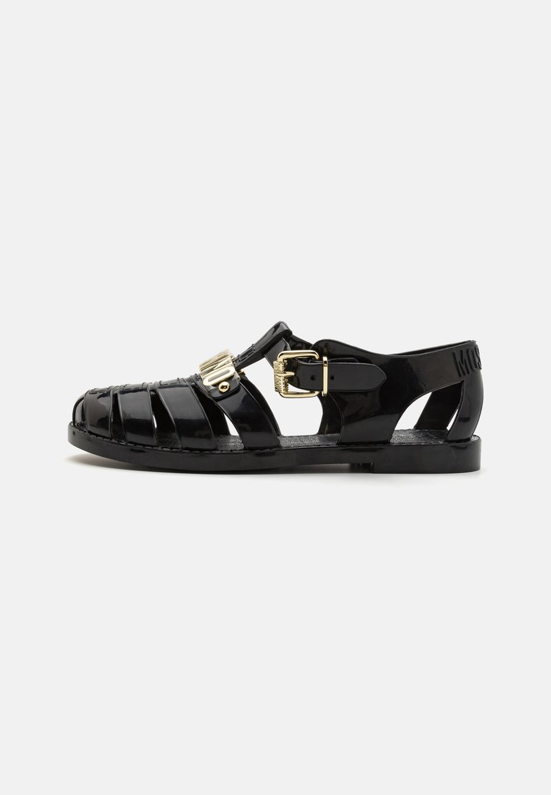 Black jelly sandals with a buckle closure, a textured upper featuring horizontal and vertical cutouts, and a flat sole.
