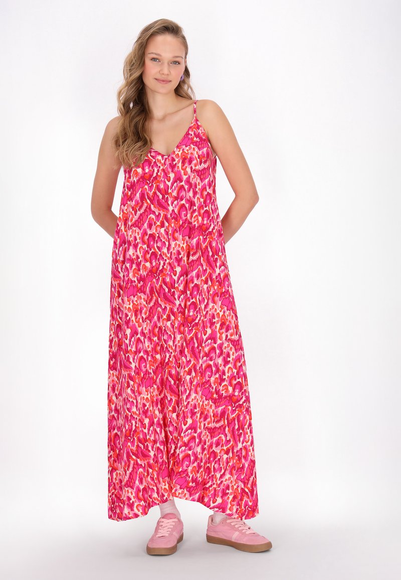 Maxi jurk in het roze met een levendig abstract patroon, voorzien van dunne bandjes en een losse pasvorm. Gecombineerd met roze sneakers.