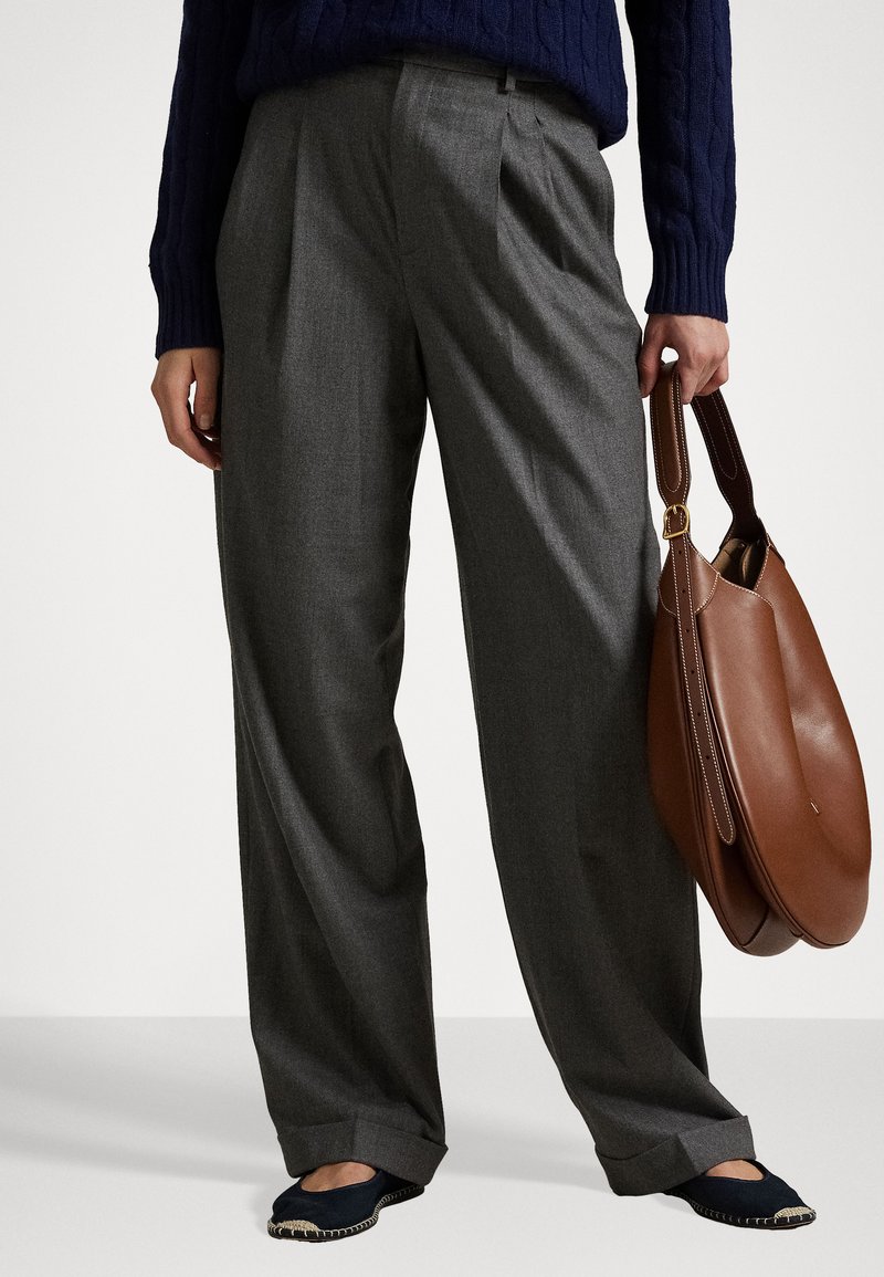 Graue, gefaltete Hosen mit taillierter Passform und glatter Textur. Kombiniert mit einem marineblauen Pullover und einer braunen Ledertasche.