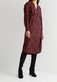 Abito a righe rosse e nere con scollatura a V, maniche lunghe e vita legata. Abbinato a stivali al ginocchio in suede nero.