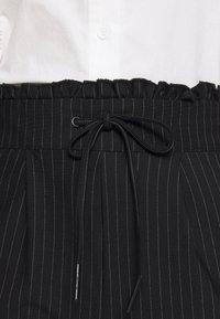 Tecido preto riscado com cintura franzida, fecho frontal ajustável e design pregueado. Visual texturizado e ajustado adequado para vestuário formal.