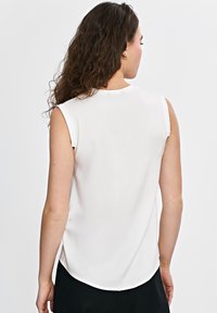 Biała bezrękawnikowa bluzka z zaokrąglonym dołem i gładką teksturą. Widok z tyłu ukazuje subtelne detale na ramionach i czysty dekolt.