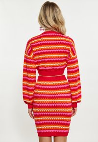 Abito lavorato a maglia con strisce zigzag rosse, rosa e arancioni, con vita aderente e maniche a palloncino. Texture liscia con dettagli a costine.