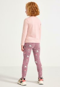 Rosa långärmad topp som kombineras med lila leggings med ett Hello Kitty-mönster. Outfiten inkluderar avslappnade sneakers med detaljer.