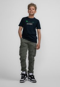 Marine t-shirt met groen en witte "Petrol Industries" grafiek, gecombineerd met olijfgroene cargobroek en zwart-witte high-top sneakers.