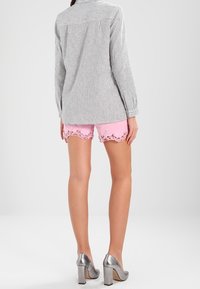 Camicia a maniche lunghe a righe in morbido tessuto, abbinata a pantaloni corti rosa con pizzo. Scarpe con tacco alto argento completano l'outfit.
