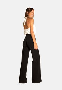 Haut à col halter blanc avec dos nu associé à un pantalon large noir taille haute, présentant un tissu lisse et une silhouette fluide.