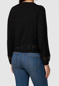 Black sweater with long sleeves, featuring a lace trim at the hem and cuffs. The design is simple and fitted, with a smooth texture.