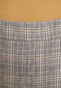 Gros plan sur un tissu côtelé jaune moutarde au-dessus d'un tissu tissé à carreaux gris et beige avec des accents noirs et blancs, montrant les détails de la texture et du motif.