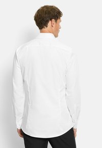 Weißes Langarmhemd aus glattem Stoff, mit klassischem Kragen, abgerundetem Saum und geknöpften Manschetten, von hinten gezeigt.