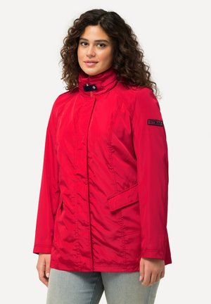 Red long-sleeve jacket with a high collar, zip closure, and side pockets. Features a smooth, lightweight fabric and a logo patch on the sleeve.