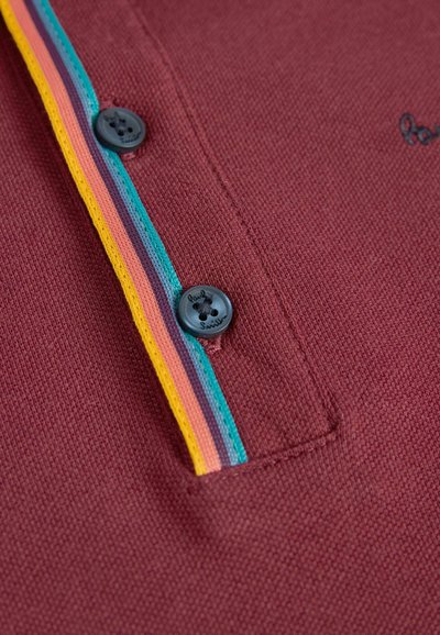 Burgundska polo majica s teksturiranim materijalom, featuring plaketom naglašenom višebojnom prugom i crnim gumbima s detaljem logotipa.