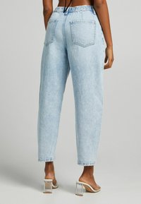Light blue high-waisted jeans with a relaxed fit, featuring two back pockets and a frayed hem. Worn with transparent block-heeled sandals.