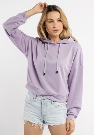 Lichtpaarse hoodie met trekkoorden en ribgebreide manchetten, gecombineerd met versleten denimshorts. De stof lijkt zacht en ontspannen.