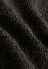 Tissu noir texturé avec un motif ondulé et strié, présentant une surface douce et duveteuse ainsi que des nuances de sombre. Idéal pour l'ameublement ou les vêtements.