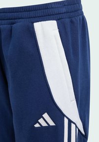 Navyblaue Sweatpants mit weichem Material, ausgestattet mit weißen Seitenstreifen und einem Adidas-Logo am unteren Bein. Mit elastischem Bund.