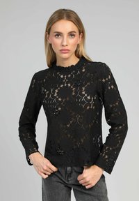 Blouse en dentelle noire à manches longues et col à volants. Motif floral avec des accents en perles pour plus de détails. Texture transparente.