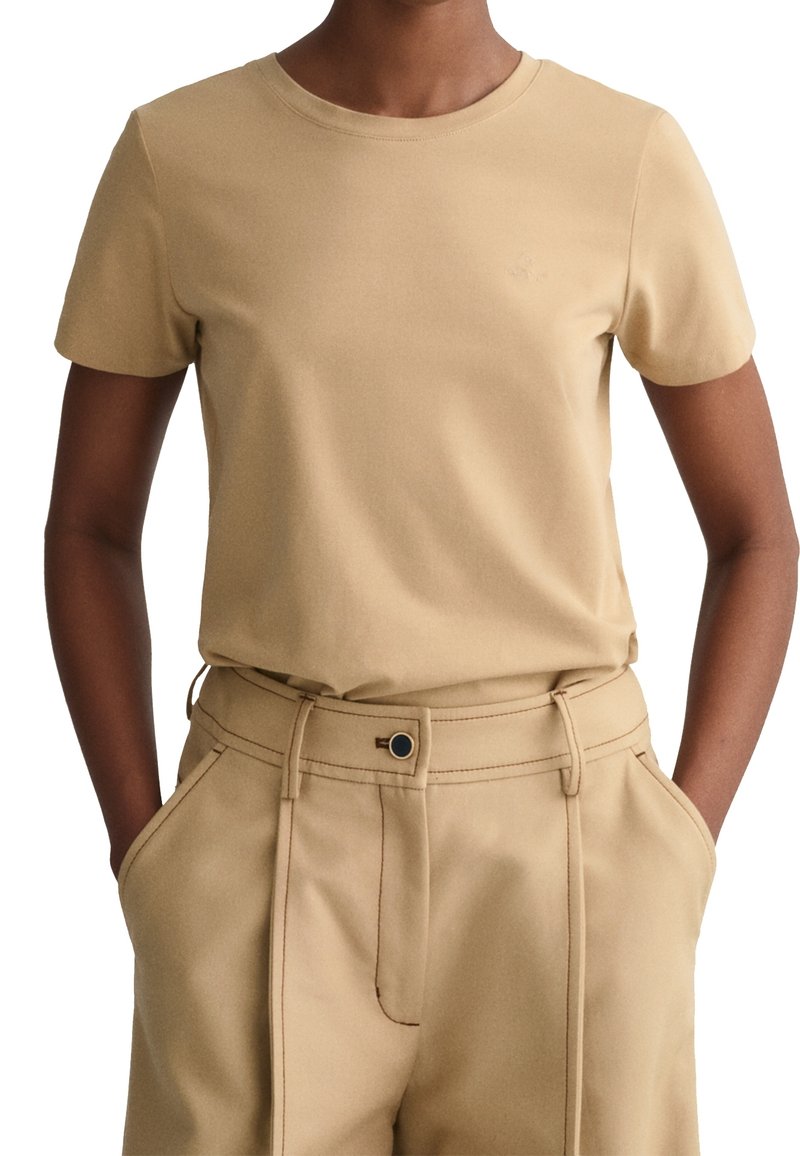 Ljusbeige t-shirt med korta ärmar, rund halsringning och mjuk textur, i kombination med matchande högmidjade byxor med sidofickor.