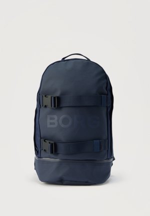 Marineblauwe rugzak met twee horizontale verstelbare riemen en clips aan de voorkant en een ritssluiting vak aan de onderkant, rechtopstaand.