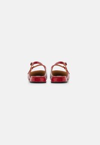 Sandales en simili cuir rouge avec une finition texturée, dotées d'une bride réglable à la cheville et d'un petit talon solide. Design ouvert au dos.