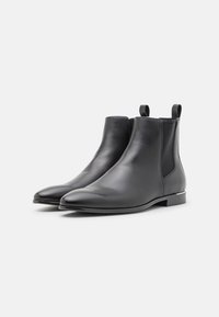 Paire de bottines basses en cuir noir élégant avec tirettes et panneaux latéraux élastiques sur un fond clair uni.