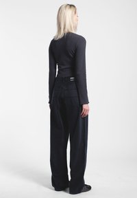 Musta ribattua pitkähihaista puseroa on yhdistetty leveälahkeisiin mustiin housuihin, joissa on takataskut ja teksturoitu pinta. Yksinkertainen ja toiminnallinen muotoilu.