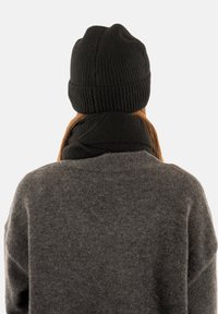 Black ribbed knit beanie and matching black scarf worn over a dark gray sweater, viewed from the back. Soft texture; simple design.