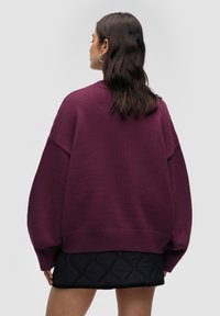 Bordeaux oversized trui van textuurstof met verlaagde schouders, gecombineerd met een zwarte gewatteerde rok met geribbelde zoomdetails.