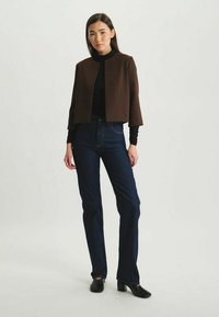 Veste brune courte en tissu lisse, assortie à un col roulé noir et un jean bleu foncé taille haute. Des chaussures à talons noires complètent le look.