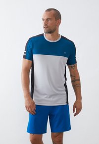 Herre sportstrøye i blå, grå og svart, med rund hals og korte ermer. Glatt tekstur med et subtilt design. Kombinert med blå shorts.