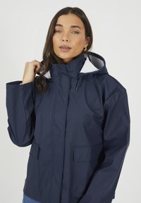 Granatowa wodoodporna kurtka z białą podszewką w kapturze, z przodu na zamek błyskawiczny oraz dwoma bocznymi kieszeniami. Gładka faktura i luźny krój o eleganckim designie.