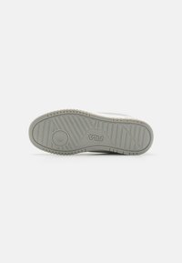 Fehér sneaker talp texturált szürke gumival, jellegzetes barázdázottsággal és egy kör alakú logóval a közepén.