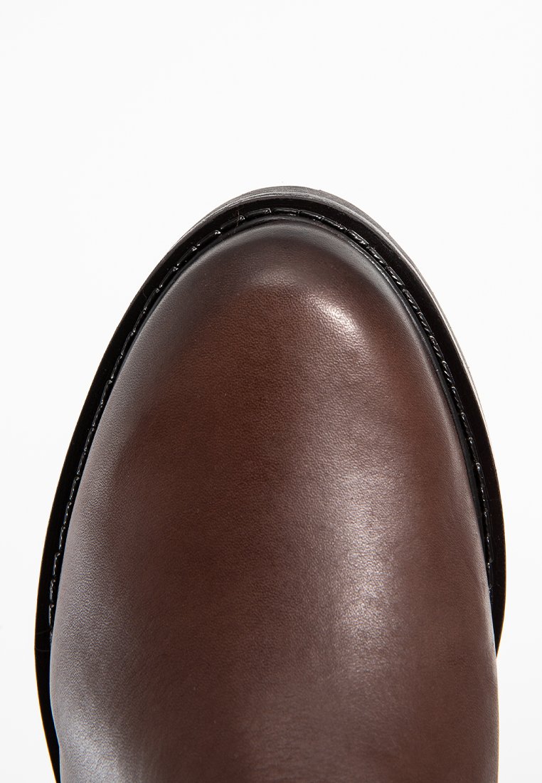 Brauner Leder-Schuh mit schwarzem genähtem Rahmen und glatter, polierter Oberfläche auf weißem Hintergrund.