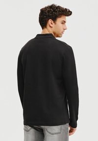 Czarny longsleeve polo z kołnierzykiem. Miękka, gładka tkanina, proste wykończenie i minimalistyczny design. Widok z przodu nie jest widoczny.