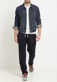 Denimjacka i mörkblått med ljusgrå krage, vit t-shirt, marinblå sweatpants och grå sneakers med bruna snören. Avslappnad outfit.