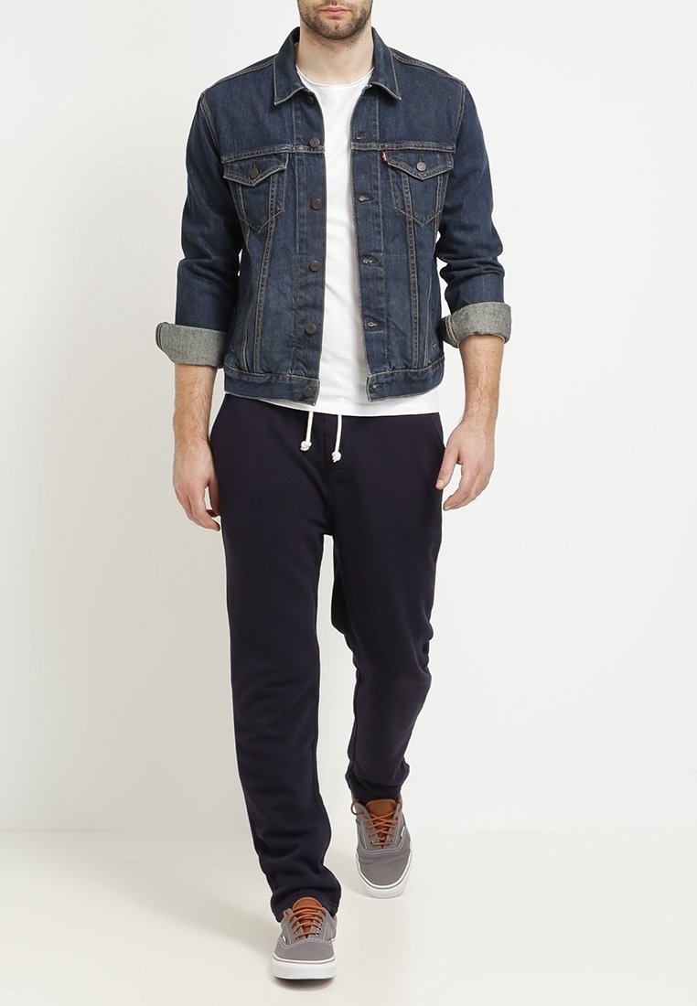 Denimjacka i mörkblått med ljusgrå krage, vit t-shirt, marinblå sweatpants och grå sneakers med bruna snören. Avslappnad outfit.