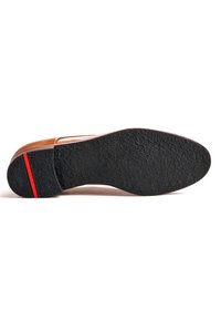 Suola di scarpa in pelle marrone con superficie in gomma nera texture. Presenta una striscia accentata rossa vicino al tallone per un tocco di dettaglio in più.