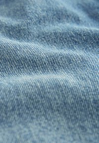 Heleda helesinise denimi kangas sujuva tekstuuriga, millel on peen twill-kude ja veidi kulunud välimus. Suurendatud pilt rõhutab kude detaile.