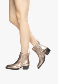 Bottines métalliques en bronze avec une finition textur�ée, un petit talon bloc et des détails de couture verticaux. Onglets de tirage pour un enfilage facile.
