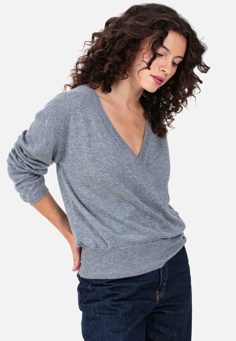 Pull gris à col en V en matière douce, avec manches longues et taille ajustée, associé à un jean denim foncé.
