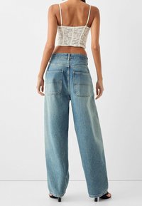 Džínové kalhoty s širokými nohavicemi v světlém modrém odstínu, s vysokým pasem, dvěma zadními kapsami a volným střihem. Povrch vypadá hladce s mírným zesvětlením.