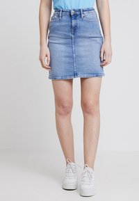 Jeanskjol i ljusblå tvätt, med rak passform, framknappslås och sidofickor. Bärs med en enfärgad blå topp och vita sneakers.