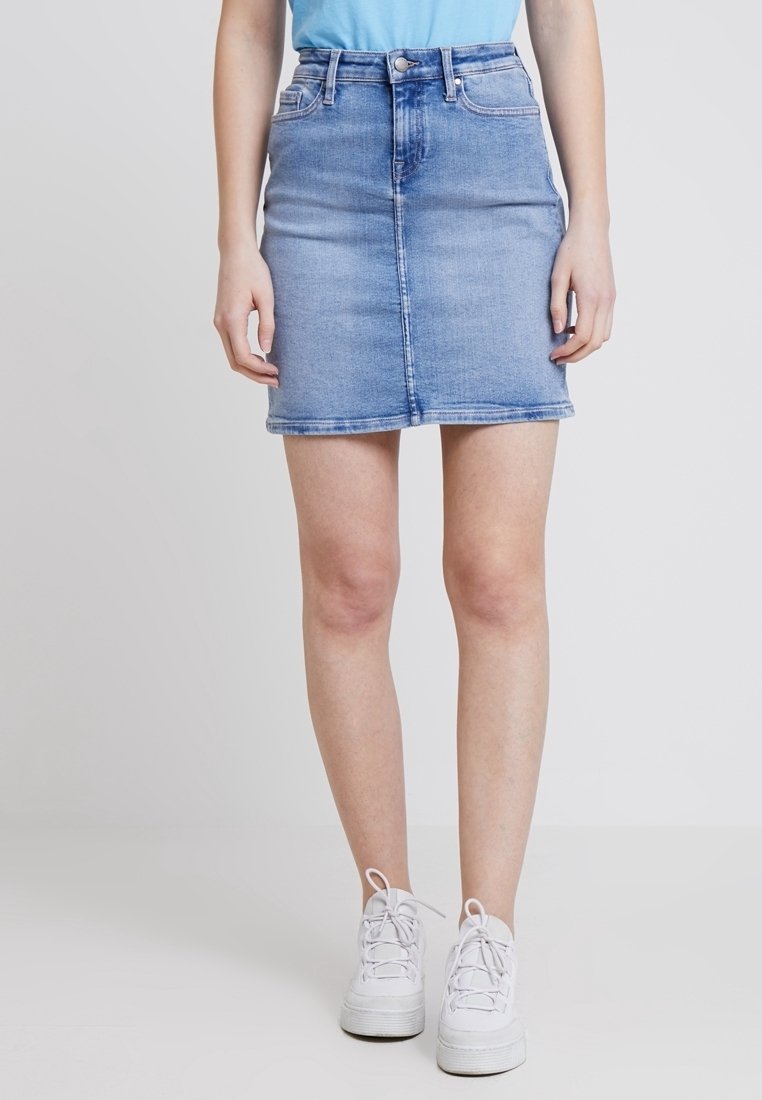 Jeanskjol i ljusblå tvätt, med rak passform, framknappslås och sidofickor. Bärs med en enfärgad blå topp och vita sneakers.